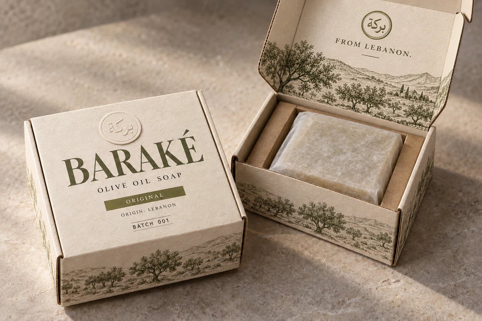 The Baraké box, cream card printed in olive green with olive groves and hills, open to show one square bar in its paper wrap, with From Lebanon inside the lid.